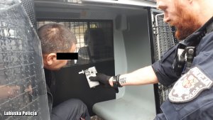 policjant badający alkomatem osobę zatrzymaną w radiowozie