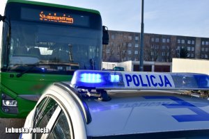 radiowóz Policji z włączonymi sygnałami świetlnymi, za nim autobus